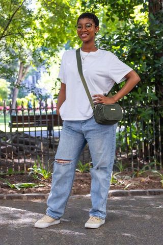 Confident african woman smiling in park wearing casual white tee and relaxed jeans