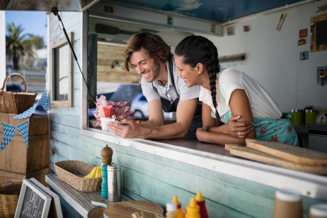 Waitstaff at a food truck smiling and interacting at the counter. Ideal for illustrating teamwork, customer service, and the casual, friendly atmosphere of street food vendors. Suitable for use in marketing materials for food trucks, hospitality training, and small business promotions.