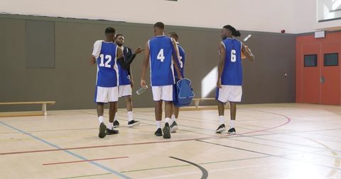 Basketball team huddling on indoor court in blue jerseys carrying bag and water bottle