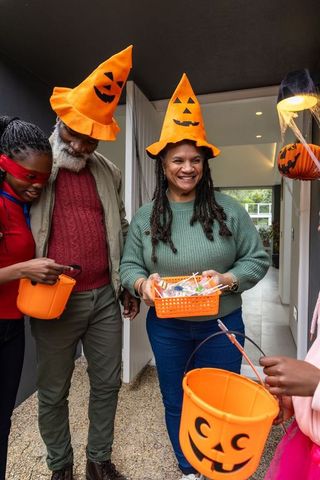 African american family wearing pumpkin hats handing out halloween candy at front door