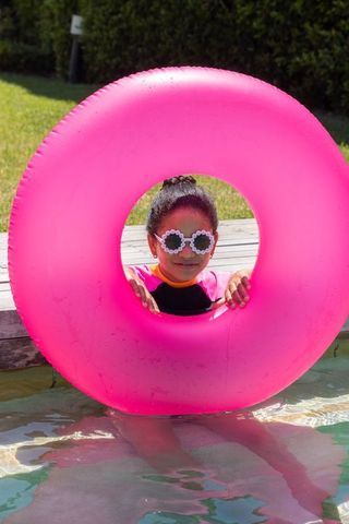 African american preteen girl peeking through pink inflatable swim ring at backyard pool