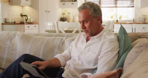 Middle-aged Man Relaxing on Sofa Using Tablet at Home