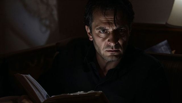 Moody late night reading under lamp light, intense man holding notebook in armchair