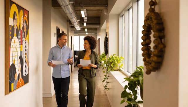 Two colleagues walking and discussing documents in modern office corridor with plants