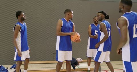 Basketball players discussing strategy during timeout on indoor court holding ball