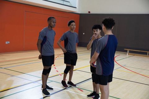 African american teen athletes huddling in school gym holding ball wearing knee pads