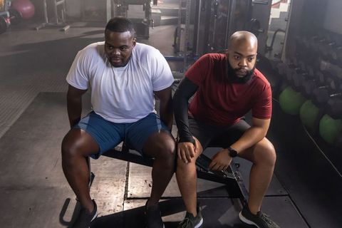 Two african men resting between sets on bench at gym strength training session and teamwork