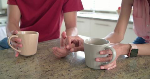 Couple holding hands over coffee mugs on kitchen counter morning intimacy and connection