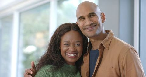 Smiling couple sharing warm embrace by sunlit windows, casual indoor lifestyle portrait