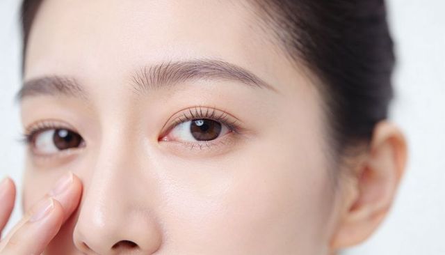 Close-up asian woman touching nose showing flawless skin, right eye detail and brows