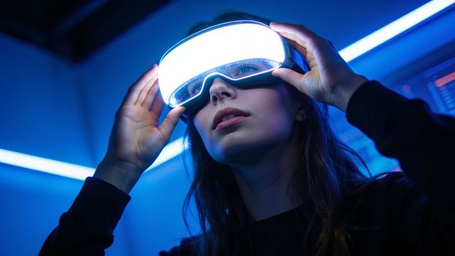 Woman adjusting illuminated vr headset in neon blue demo, futuristic wearable technology