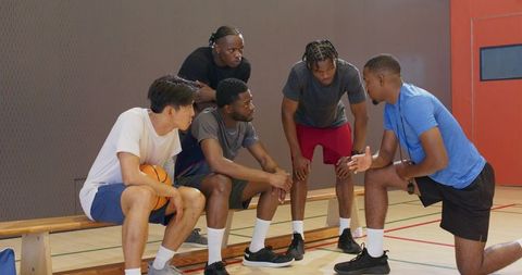 Coach delivering focused pregame huddle with diverse basketball team listening on bench