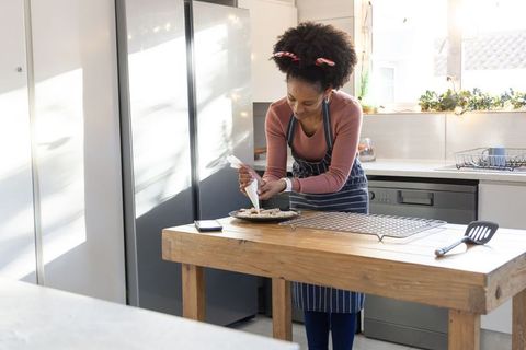 African american woman decorating tart with piping bag in sunlit home kitchen