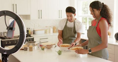 African american couple cooking and recording pasta tutorial in bright modern kitchen