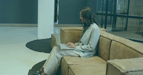 Professional woman typing on laptop in modern coworking lounge wearing tailored suit