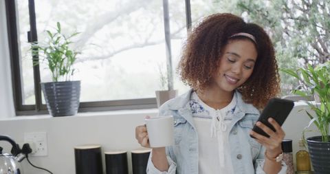 Happy Woman Enjoying Coffee While Using Smartphone in Modern Kitchen