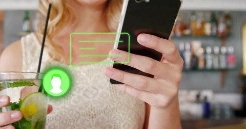 Woman holding smartphone and sipping cocktail with neon chat overlay in bar