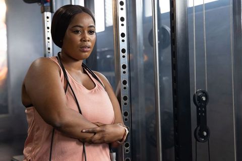 Confident african american woman leaning on power rack at gym wearing peach tank