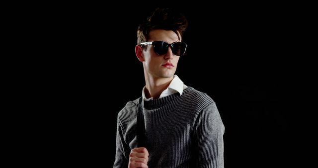 A young Caucasian male models a pair of sunglasses and a casual sweater, with copy space. His confident pose and stylish attire suggest a fashion-oriented theme.