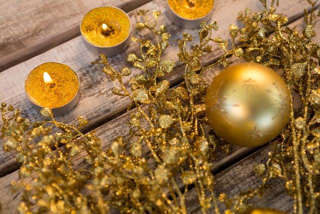 Golden Christmas decorations, including candles and an ornament, arranged on a wooden plank. Perfect for holiday-themed promotions, festive greeting cards, seasonal blog posts, and social media content celebrating the warmth and joy of Christmas.