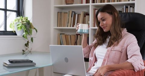 Professional Woman Sipping Coffee While Working on Laptop at Home Office