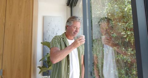 Mature man enjoying morning coffee by sliding glass door with gentle natural light