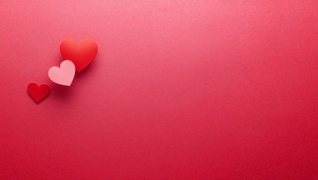 Three paper hearts aligning diagonally on red textured background with copy space