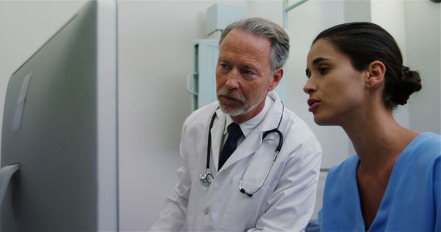 Medical professionals consulting on patient diagnosis. Old doctor with stethoscope and young nurse collaborate, looking at computer screen. Useful for healthcare teamwork, hospital workflow, medical consulting, unified patient care.