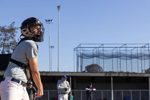 Baseball Catcher Wearing Helmet and Chest Protector Watching Pitch in Sunny Ballpark