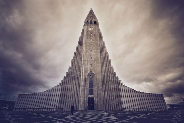 Hallgrímskirkja church photographed from ground level with a dramatic cloudy sky. This iconic gothic building is located in Reykjavik, Iceland. Suitable for articles on architecture, travel guides, cultural content, or religious publications.