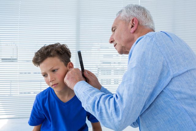 Doctor examining young boy's ear in a clinic, focusing on ear health. Useful for medical, healthcare, pediatric care, and health education materials. Highlights professional medical care and patient interaction.
