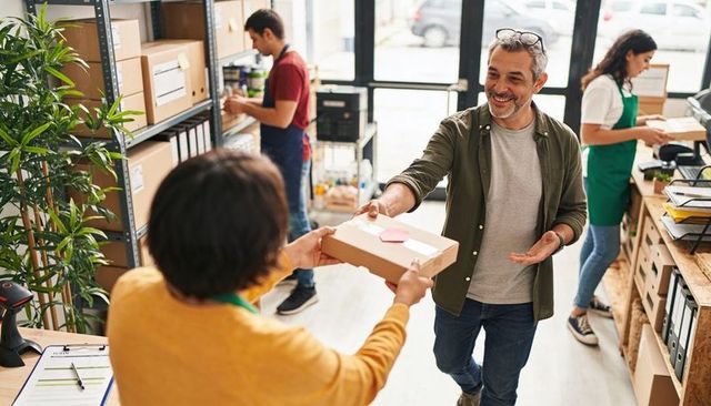 Senior customer receiving parcel at local store counter, friendly retail pickup
