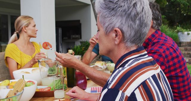 Caucasian senior woman turning and smiling during family celebration meal in garden. three generation family celebrating independence day eating outdoors together.