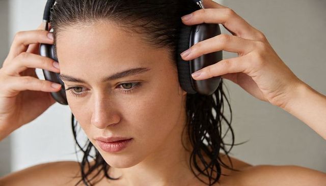 Woman adjusting over-ear headphones with wet hair and bare shoulders, calm focused portrait