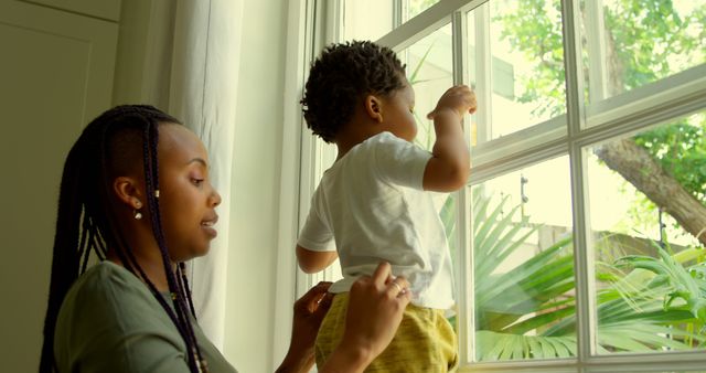 Mother holding young son while looking out window on sunny day - Download Free Stock Images Pikwizard.com