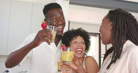 African american friends laughing and toasting with strawberry drinks in modern kitchen