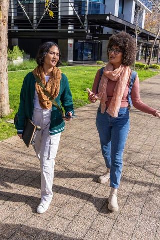 Female students walking and talking on campus carrying tablet and skateboard