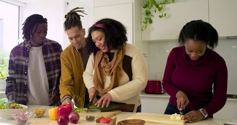 Diverse friends preparing healthy meal at modern kitchen island chopping vibrant produce
