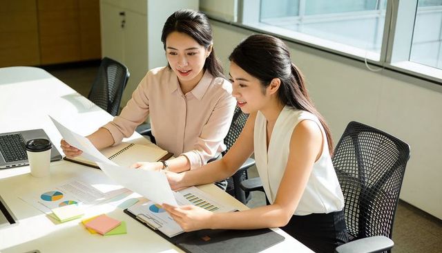 Asian businesswomen collaborating over charts and graphs in bright modern office workspace
