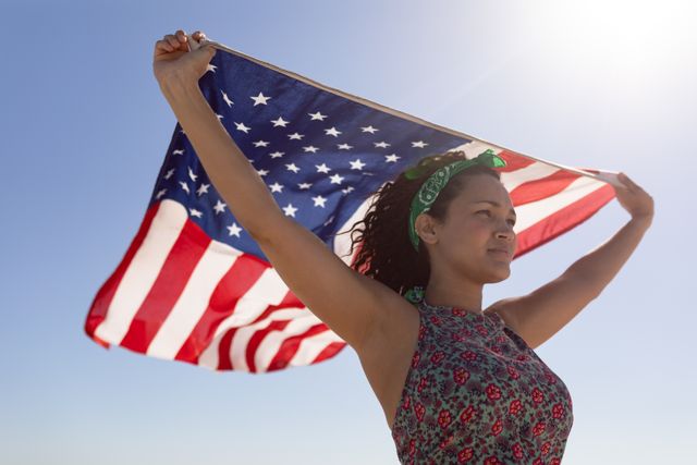 Young woman waving American flag on a sunny beach, symbolizing patriotism and freedom. Ideal for use in content related to national holidays, summer celebrations, travel, and outdoor activities. Perfect for promoting American pride and independence.
