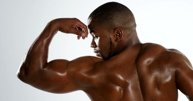An African American man showcases his muscular physique by flexing his bicep, with copy space. His focused expression and impressive build emphasize dedication to fitness and strength training.