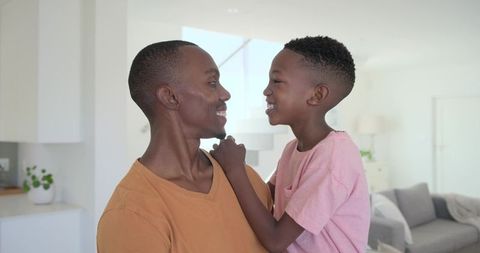 Father holding smiling son, sharing warm moment in bright modern living room with daylight