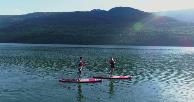 Couple Paddleboarding on Serene Lake Against Scenic Mountain Backdrop - Download Free Stock Images Pikwizard.com