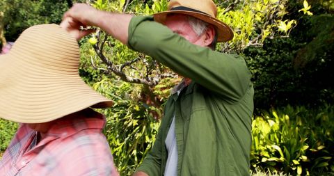 Senior couple playing with wide-brim hats in garden