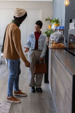African american friends chatting at cafe counter with pastry display and handbag