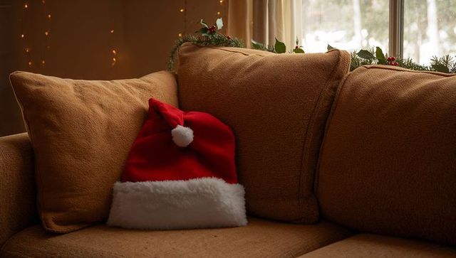 Cozy christmas santa hat on brown sofa with garland, berries and warm lights