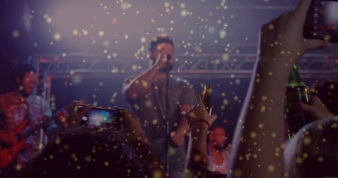 Lead vocalist performing to cheering crowd with phones, confetti and stage spotlights