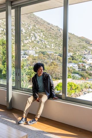 African american man sitting on wide windowsill enjoying sunlit interior with hillside view