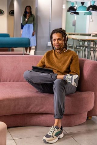 African american coworkers sitting on pink sofa holding tablet and phone in modern coworking lounge