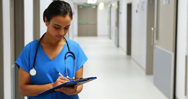 Female healthcare worker writing patient notes in hospital corridor - Download Free Stock Images Pikwizard.com